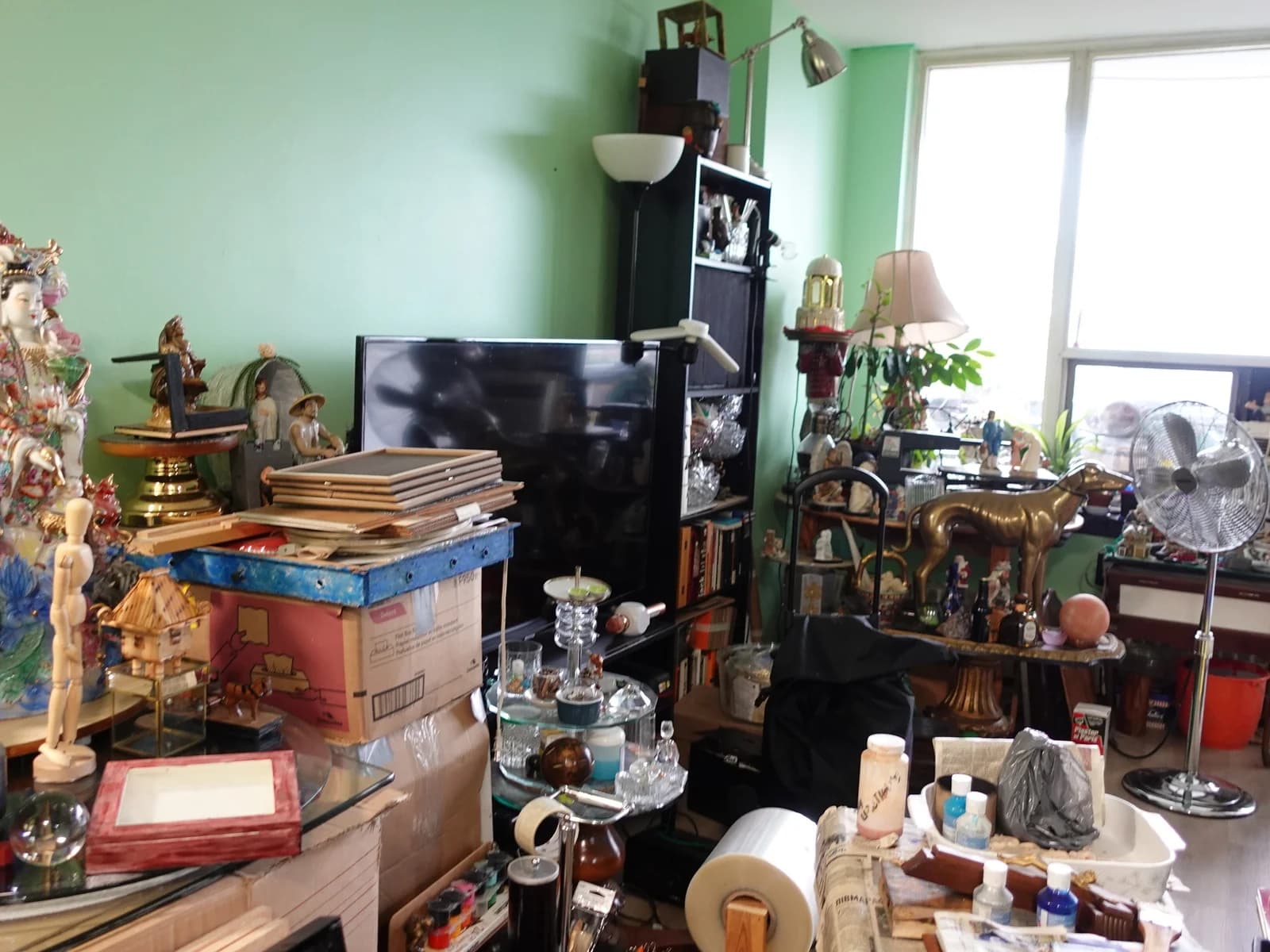 Living room before: statues, frames and boxes stacked in front of the TV and bookshelf